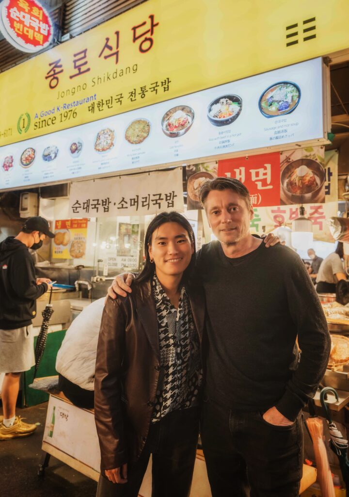 Haircut Harry Standing Outside a Restaurant with Jimmy at a Food Market in Seoul, South Korea